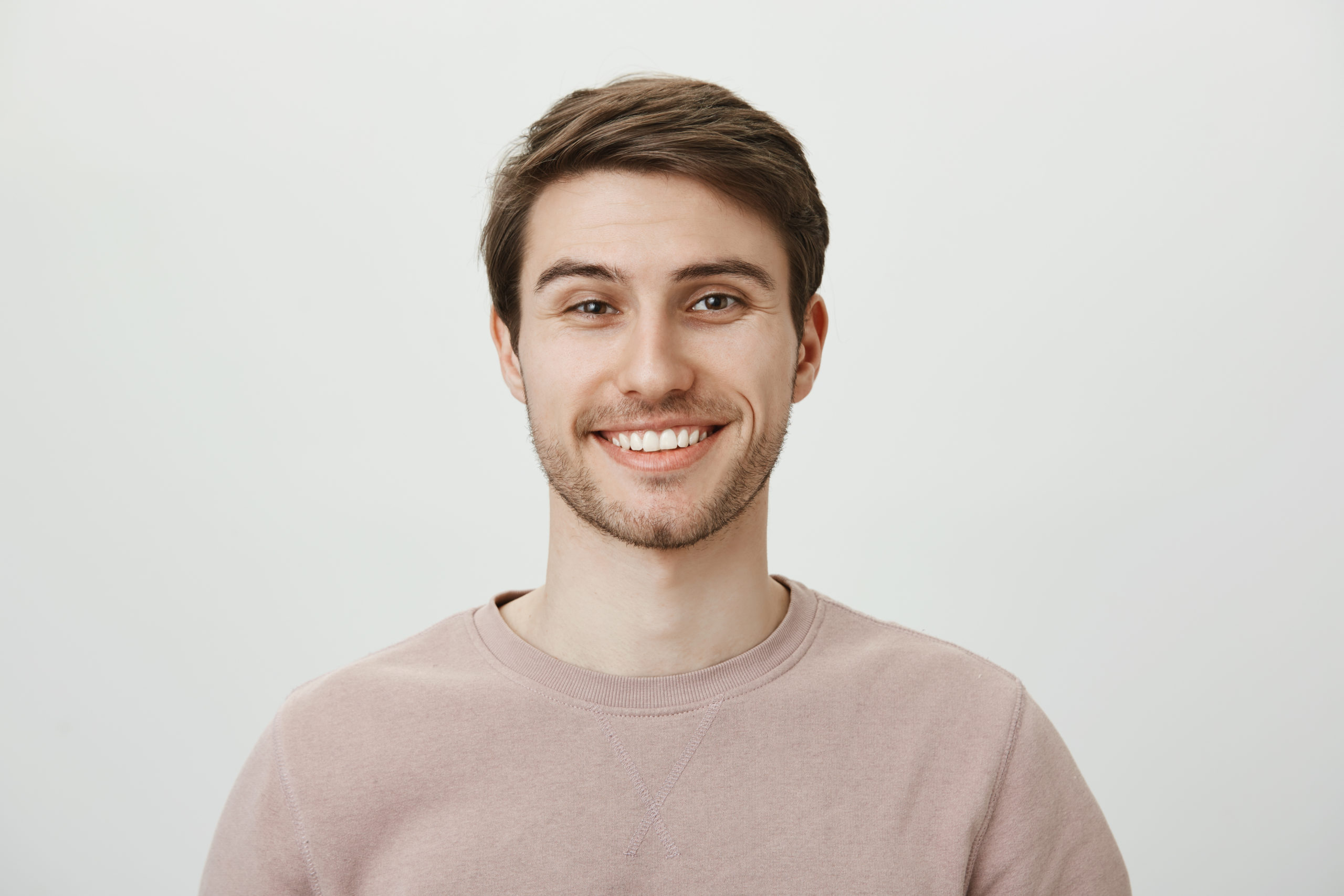 Confident attractive caucasian guy in beige pullover smiling broadly while standing against gray background, feeling self-assured while helping out customer, giving some advice about his investments.